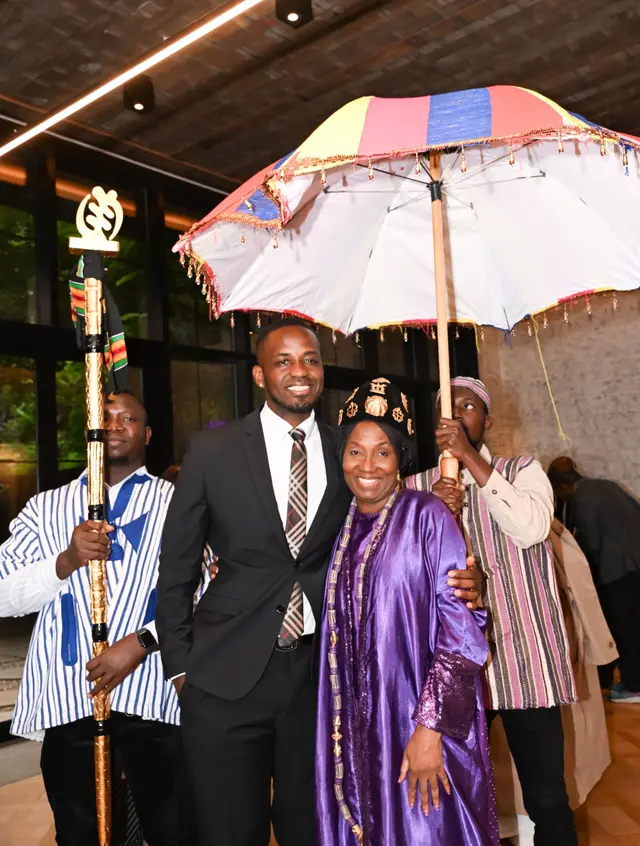 H.E. Rev. Dr. Ocansey poses with a guest beneath the ceremonial umbrella and gold staff